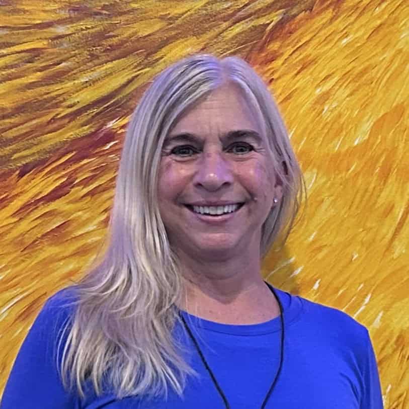 lisa-headshot Smiling woman with long blonde hair in a blue top against a yellow abstract background.